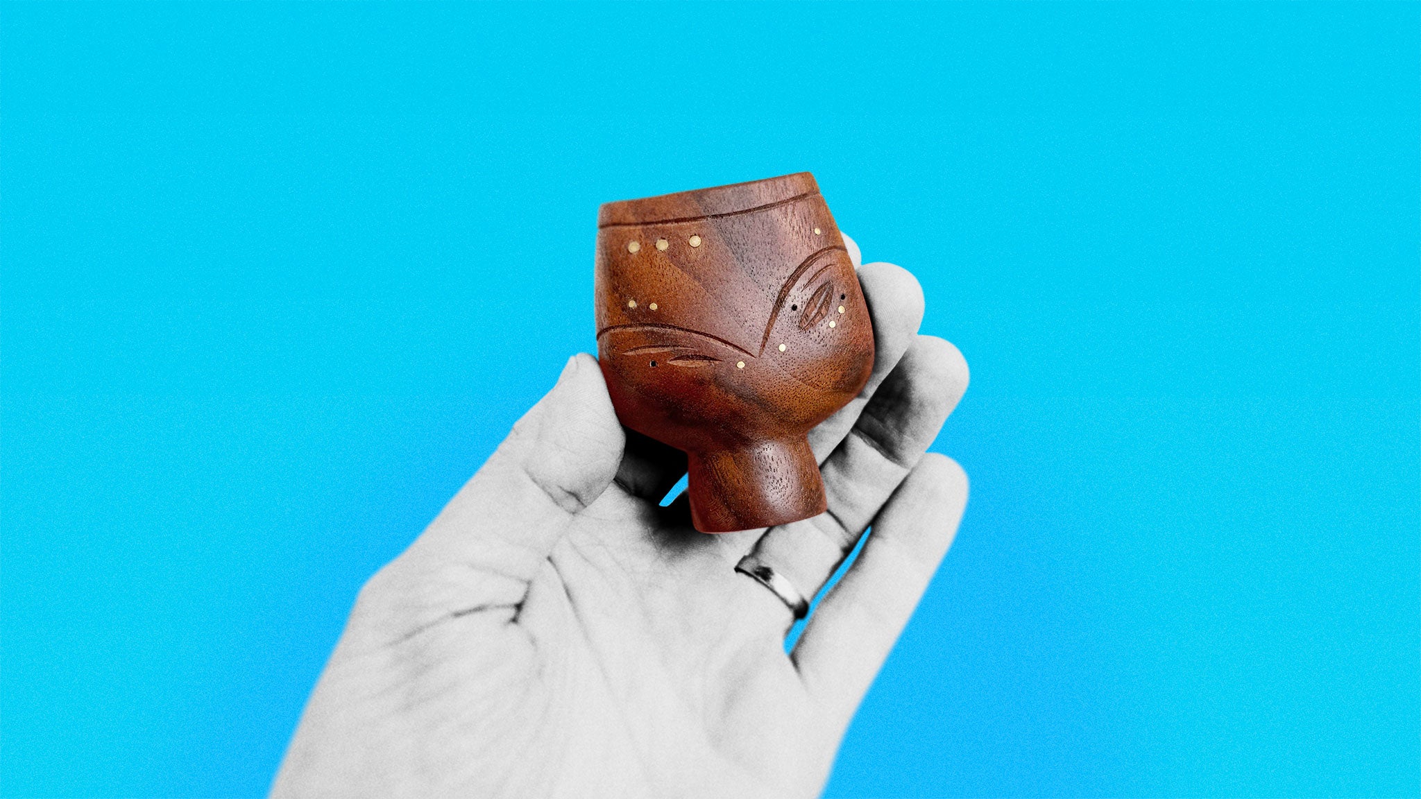 Timeless Mid-Century black walnut sculpture about 7 cm high of round figure with brass inserts held in hand on azure background