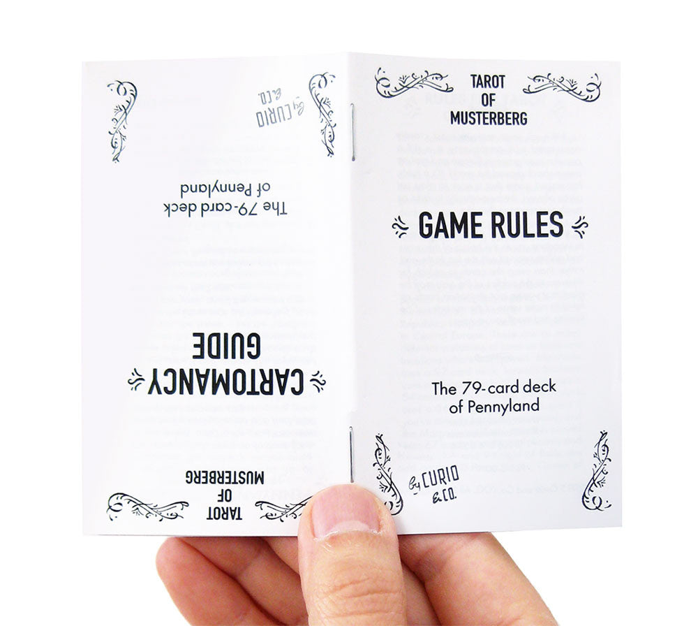 Hand holding two-sided instruction manual for the Tarot of Musterberg's game rules and cartomancy