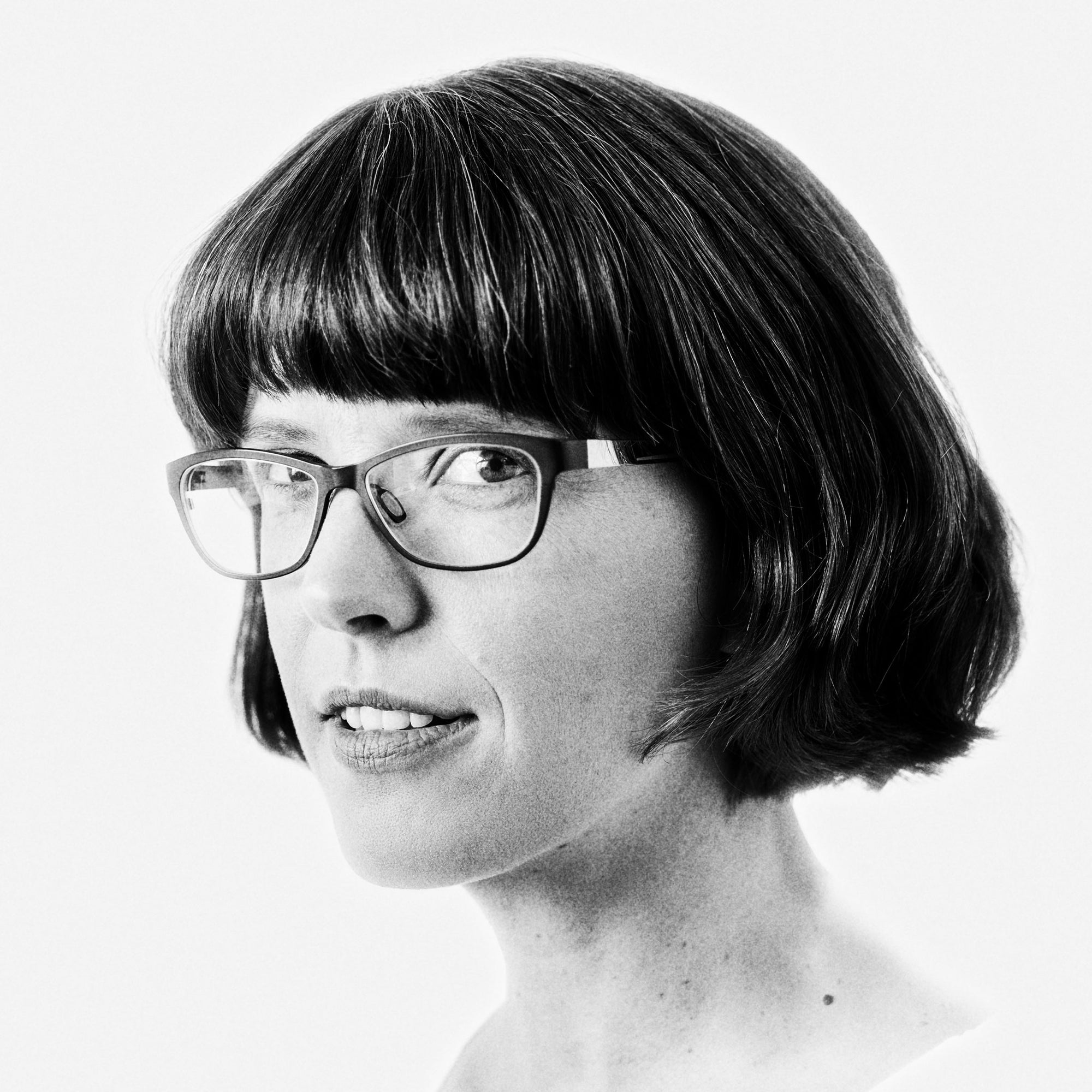 Black and white portrait of Kirstie Shepherd with bob hair and slight smile on white background.