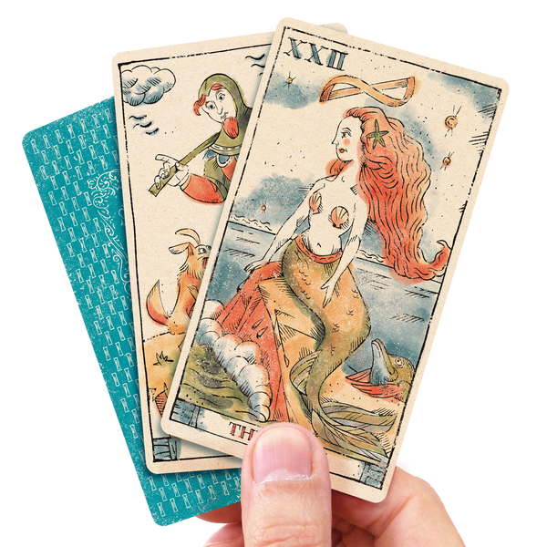 Hand holding 3 tarot cards featuring a mermaid with red hair the fool and the card's back
