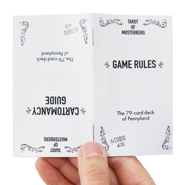 Tarot of Musterberg by Curio & Co. the 79-card deck of Pennyland game rules and cartomancy guide booklet held by a hand