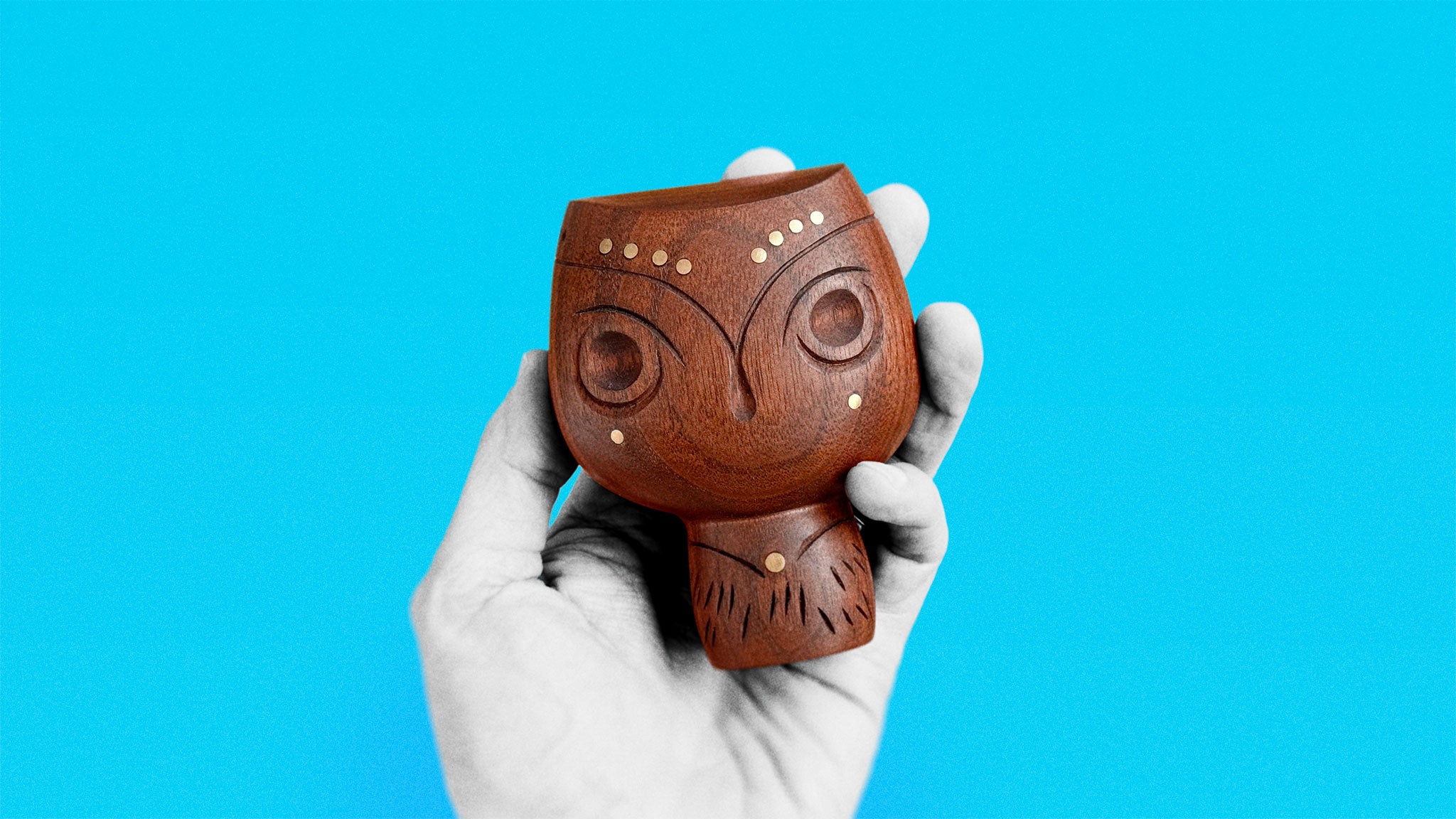 Timeless Mid-Century walnut wood sculpture of round figure with brass inserts held in hand on azure background