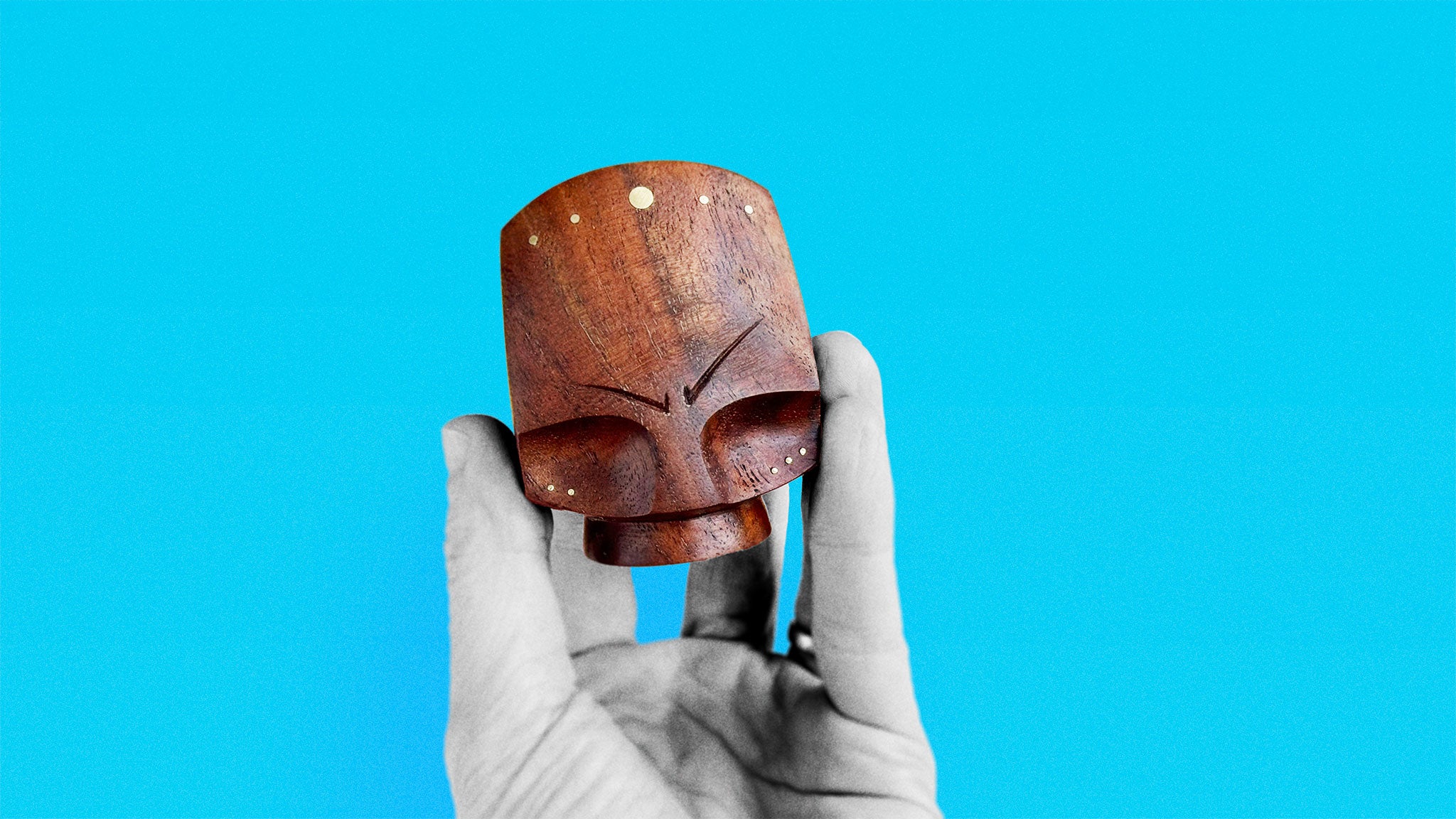 Timeless Mid-Century sculpture in black walnut about 9 cm high of abstract shaped stylized head with puzzling expression and brass inserts held in hand on azure background